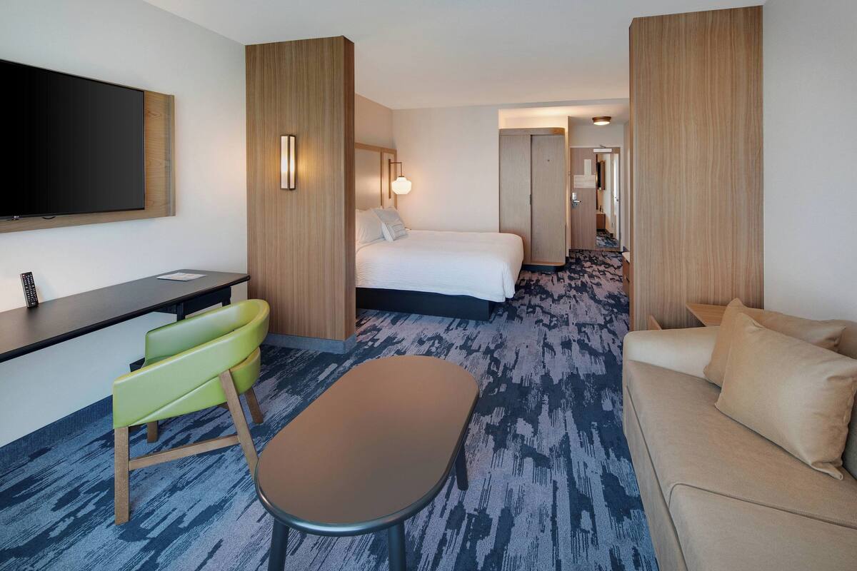 A hotel room with a bed, a desk, a green chair, a sofa, and a TV.