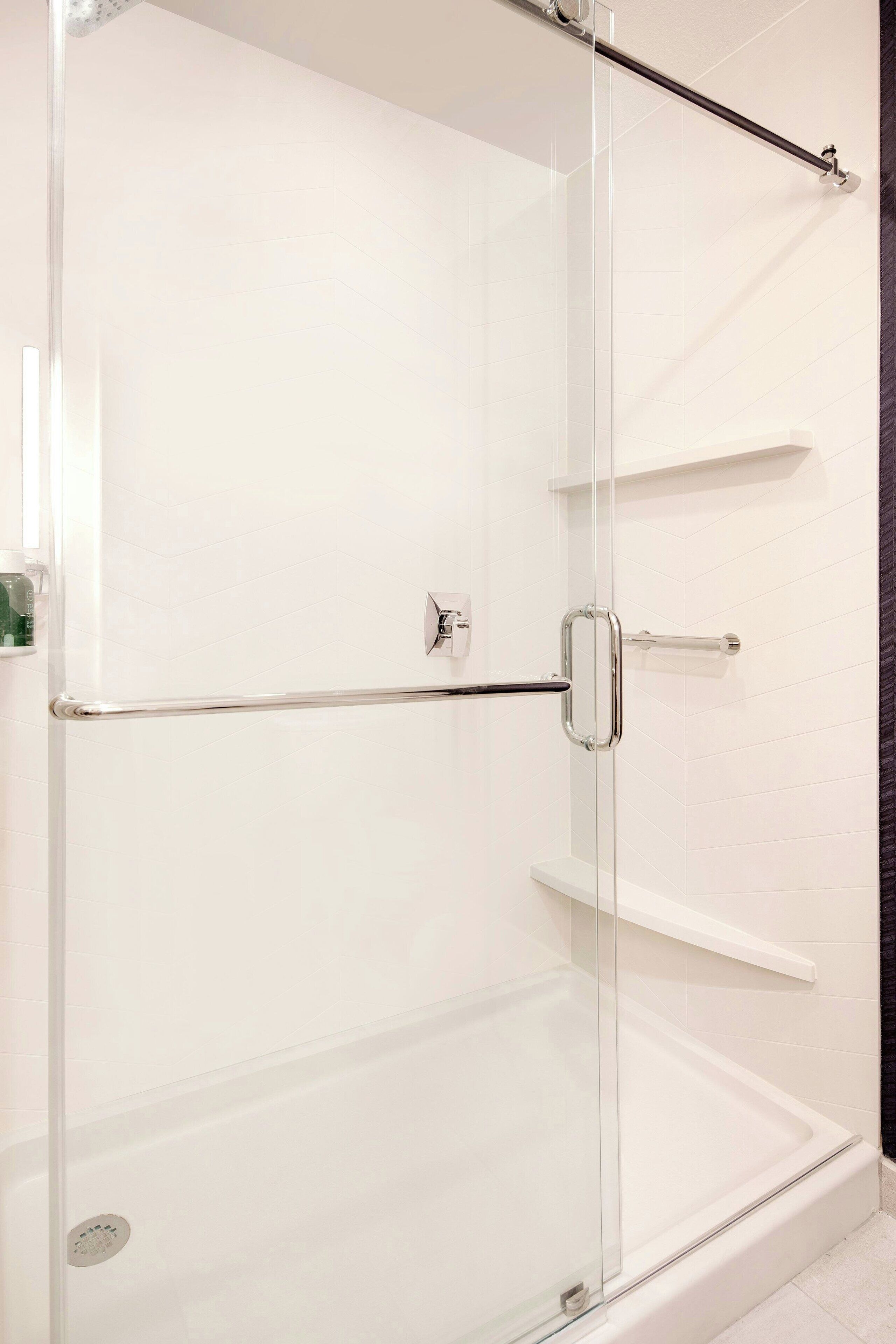 Une douche fermée par des parois en verre, dotée d’une poignée en chrome et d’une étagère.