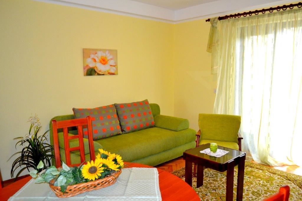 A living room with a green sofa, a red chair, a small table with a vase of flowers, and a painting on the wall.