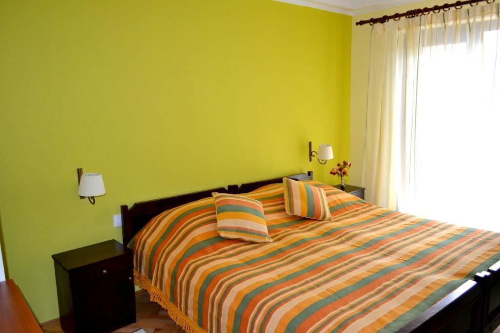 A bed with striped bedding, a nightstand, a lamp, and a window with curtains.