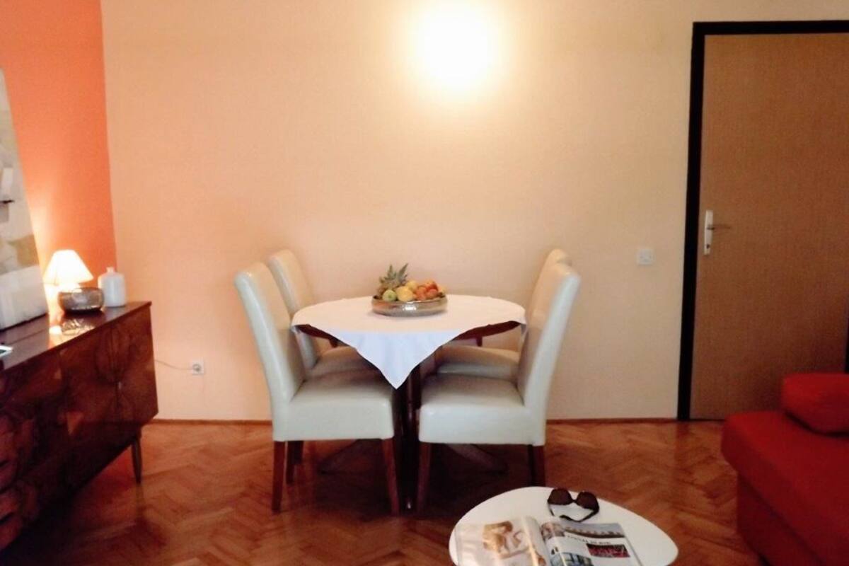 Un coin repas avec une table ronde, deux chaises, une petite table sur laquelle se trouve un saladier rempli de fruits, un meuble en bois et un canapé rouge.
