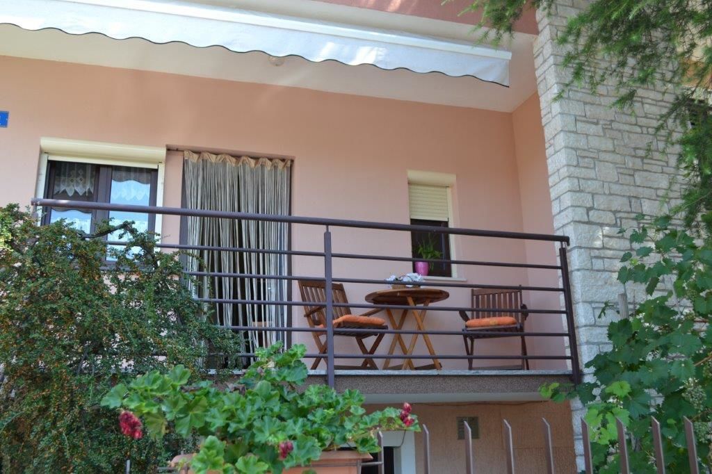 A balcony with a table and chairs, a potted plant, and a view of a building with a stone facade.