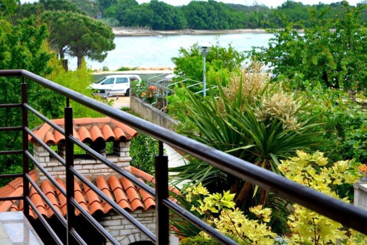 Un balcon donnant sur une étendue d’eau, entouré de verdure et surmonté d’un toit recouvert de tuiles.