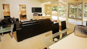 A modern living room with a black leather sofa, a glass coffee table, and a flat-screen TV mounted on the wall. - Beach House Units - 2 (Cowes)