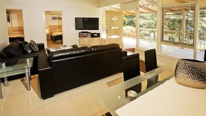 A modern living room with a black leather sofa, a glass coffee table, and a flat-screen TV mounted on the wall. - Beach House Units - 3 (Cowes)