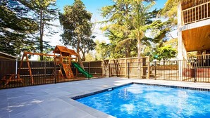 A swimming pool with a wooden play structure and a fenced area. - Beach House Units - 3 (Cowes)