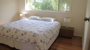 A bedroom with a bed, two bedside tables, a window, and a door. - Island Living (Cowes)
