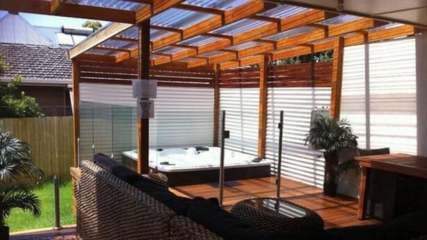 A covered outdoor seating area with a hot tub, wooden deck, and a pergola structure. - Island Living (Cowes)