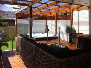 Ein überdachter Außenbereich mit Whirlpool, Holzterrasse und einer Pergola.