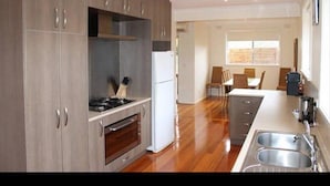 A modern kitchen with wooden cabinets, a built-in oven, a refrigerator, and a dining area with a table and chairs. - Island Living (Cowes)