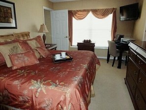 Une chambre d’hôtel avec un grand lit, un bureau, une chaise, une télévision et une fenêtre avec des rideaux.