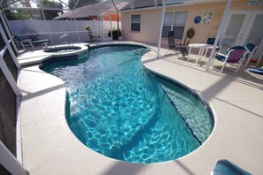 Une piscine avec un jacuzzi, entourée de chaises longues et dotée d’un patio couvert.