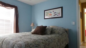 Une chambre à coucher avec un lit, un tableau encadré au mur et une fenêtre avec des rideaux.