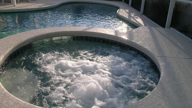 Piscina con zona de hidromasaje, rodeada por una valla blanca y sillas.