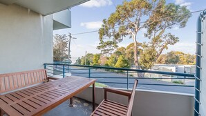 A balcony with a wooden bench and table, overlooking a road and trees. - The Waves 216 (Cowes)