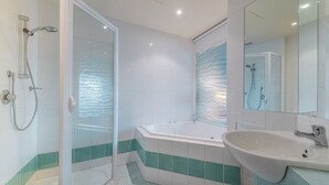 A modern bathroom with a glass-enclosed shower, a freestanding bathtub, and a sink with a mirror. - The Waves 216 (Cowes)