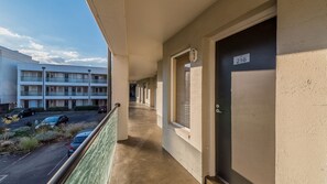 Un pasillo con un balcón, una puerta con el número 216 y un edificio con varias ventanas al fondo.