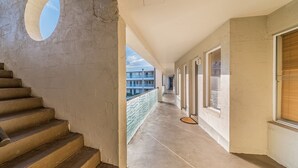 A corridor with a concrete staircase, a glass balustrade, and a view of a building in the distance. - The Waves 216 (Cowes)