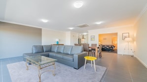 A modern living room with a grey sofa, a glass coffee table, and a yellow side table. - Thompson Avenue Apartments - 3 (Cowes)