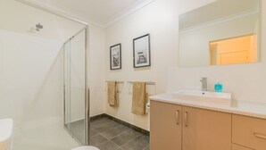 A bathroom with a glass shower enclosure, a sink with a mirror above it, and two framed pictures on the wall. - Thompson Avenue Apartments - 3 (Cowes)