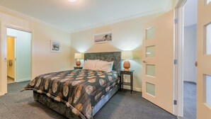 A bedroom with a large bed, two bedside tables with lamps, a headboard, and a door with frosted glass panels. - Thompson Avenue Apartments - 3 (Cowes)