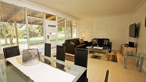 A modern living room with a glass dining table, two sofas, and a TV on the wall. - Beach House Units - 1 (Cowes)