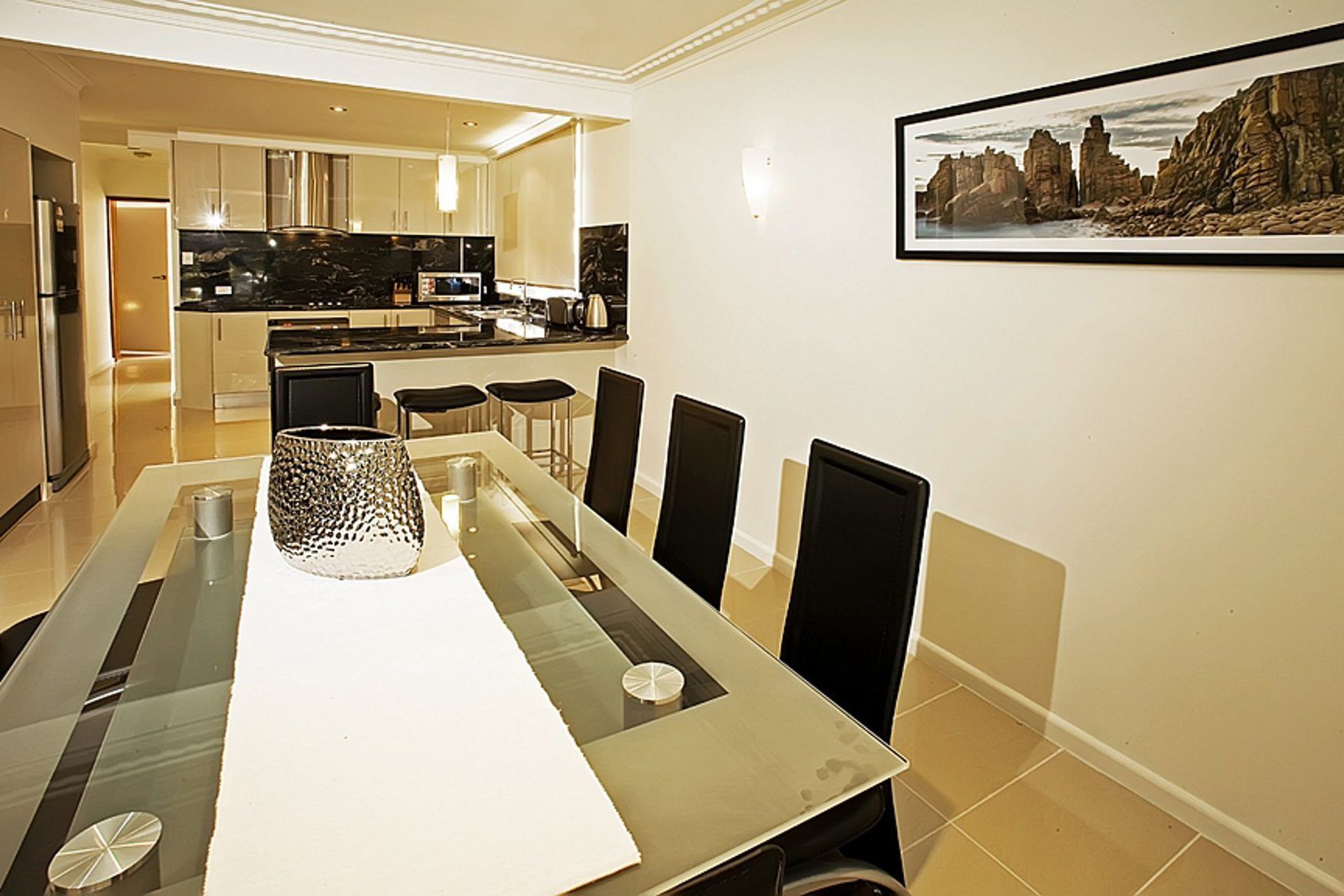 Un comedor moderno con una mesa de vidrio, sillas negras y un cuadro grande en la pared.
