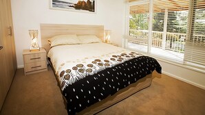 A bedroom with a bed, bedside tables, a lamp, a framed picture on the wall, and a window with blinds. - Beach House Units - 1 (Cowes)