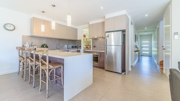 A modern kitchen with a central island, bar stools, stainless steel appliances, and pendant lighting. - Birch Holiday House (Cowes)