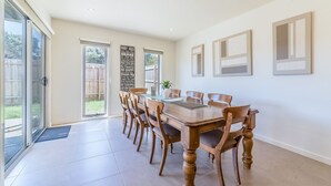 A dining room with a wooden table and chairs, a large window, and a wall with framed artwork. - Birch Holiday House (Cowes)