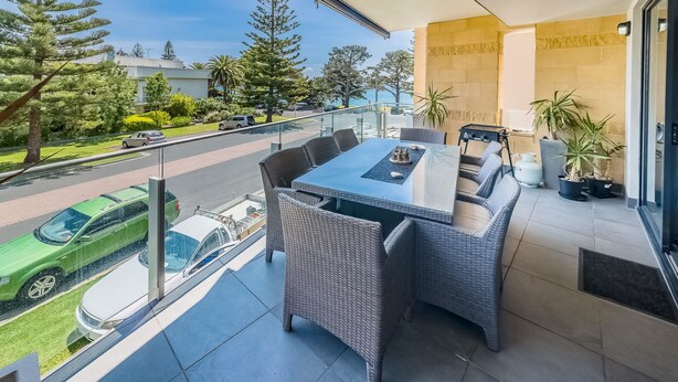 A balcony with a dining table and chairs, overlooking a street with parked cars and trees. - C-Scape by the Sea No.9 (Cowes)