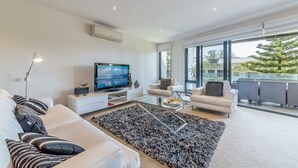 A modern living room with a flat-screen TV, white sofas, a glass coffee table, and a large window with a view of the outdoors. - C-Scape by the Sea No.9 (Cowes)