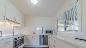 A modern kitchen with white cabinetry, stainless steel appliances, and a wooden floor. - Genesta 5B House in Cowes (Cowes)