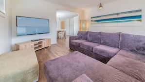 A modern living room with a large flat-screen TV, a purple sofa, a wooden coffee table, and a dining area with white chairs. - Genesta 5B House in Cowes (Cowes)
