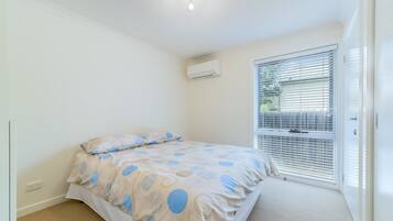 Un dormitorio con cama, ventana con persianas, unidad de aire acondicionado y suelo alfombrado.