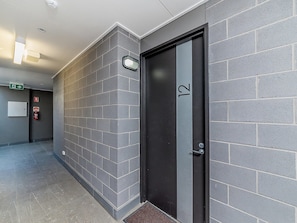 A hallway with grey brick walls, a black door with the number 12, and a fire extinguisher on the wall.