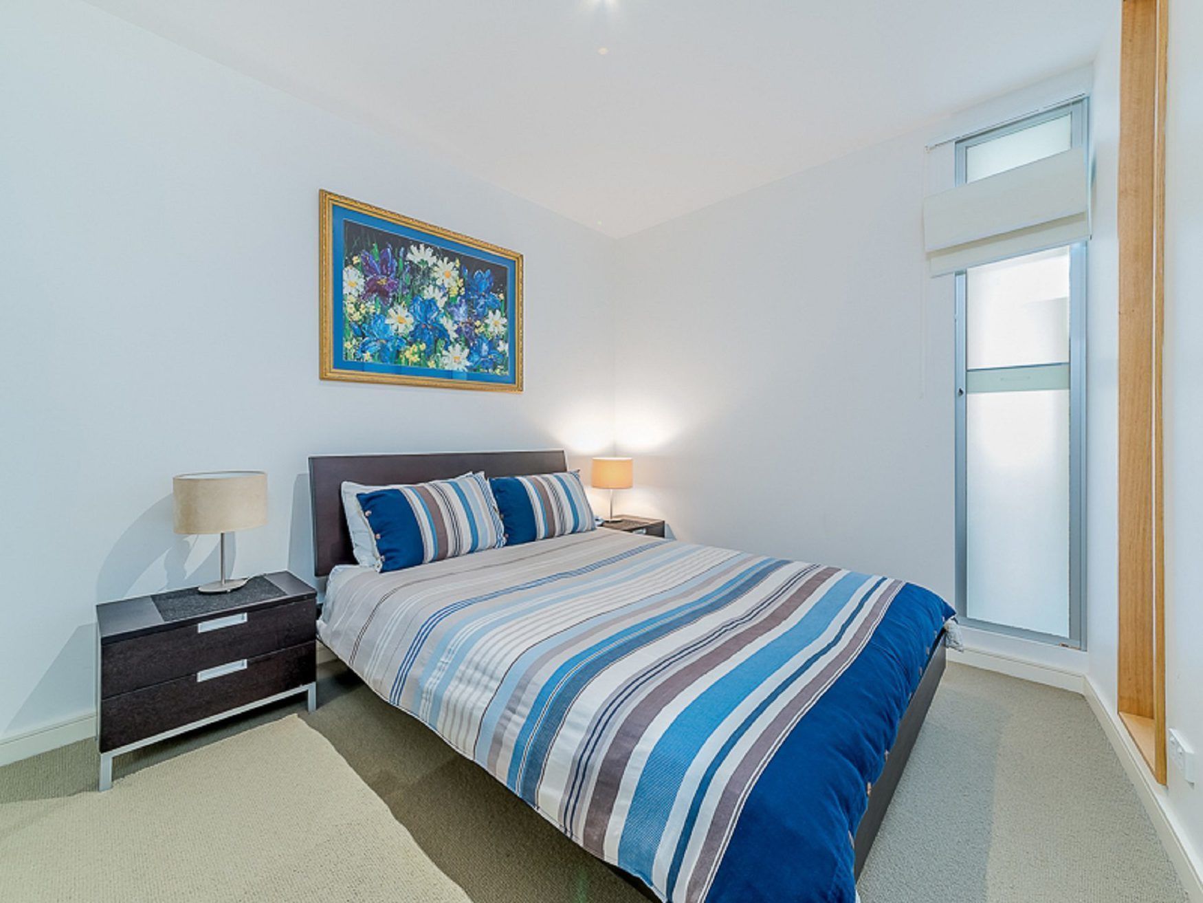 A bedroom with a bed, nightstands, a lamp, a painting, and a window.