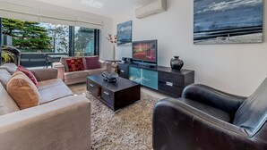 Een moderne woonkamer met een bank, een salontafel, een televisie en een schilderij aan de muur.