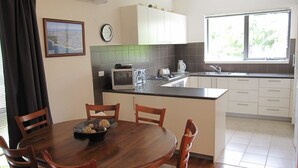 Cozinha moderna com área de jantar, apresentando uma mesa de madeira, cadeiras, micro-ondas e uma pia.