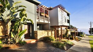 Uma casa moderna de dois andares com fachada de pedra, varanda e vista para o oceano.