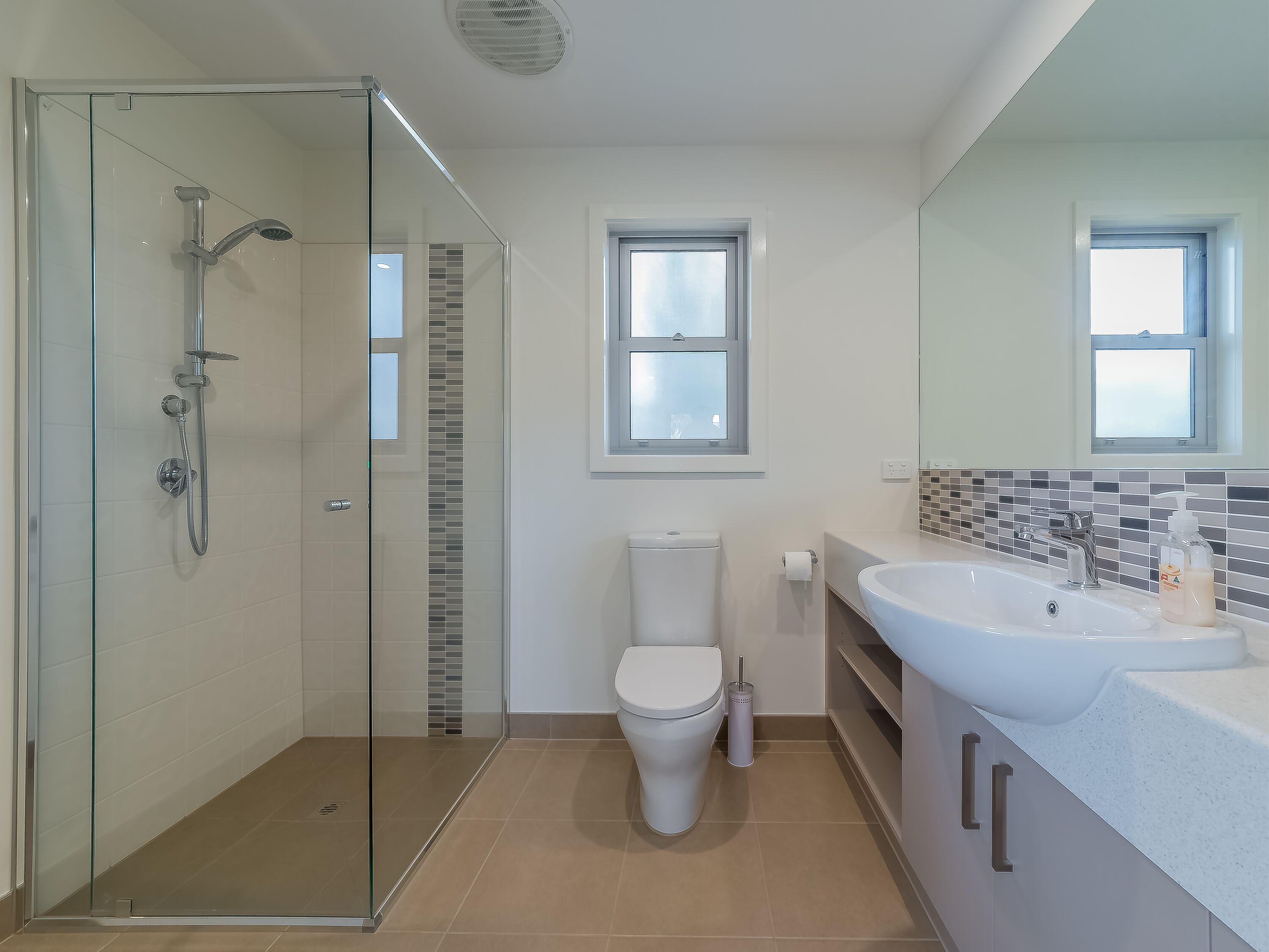Une salle de bain moderne avec une douche à parois de verre, des toilettes et un lavabo avec un miroir au-dessus.