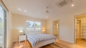 Un dormitorio con cama, mesitas de noche, ventana, ventilador de techo y vestidor.