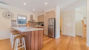 Una cocina moderna con una isla central, taburetes de madera, electrodomésticos de acero inoxidable y un ventanal grande.