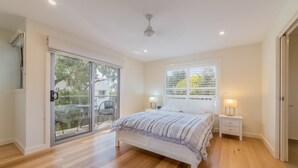Un dormitorio con cama, mesitas de noche, una ventana y puertas de cristal correderas a un balcón.