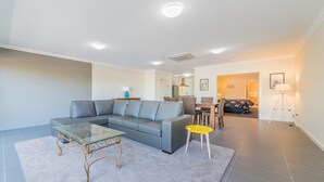 Ein modernes Wohnzimmer mit einem grauen Ecksofa, einem Glastisch und einem Essbereich mit einem Holztisch und Stühlen.