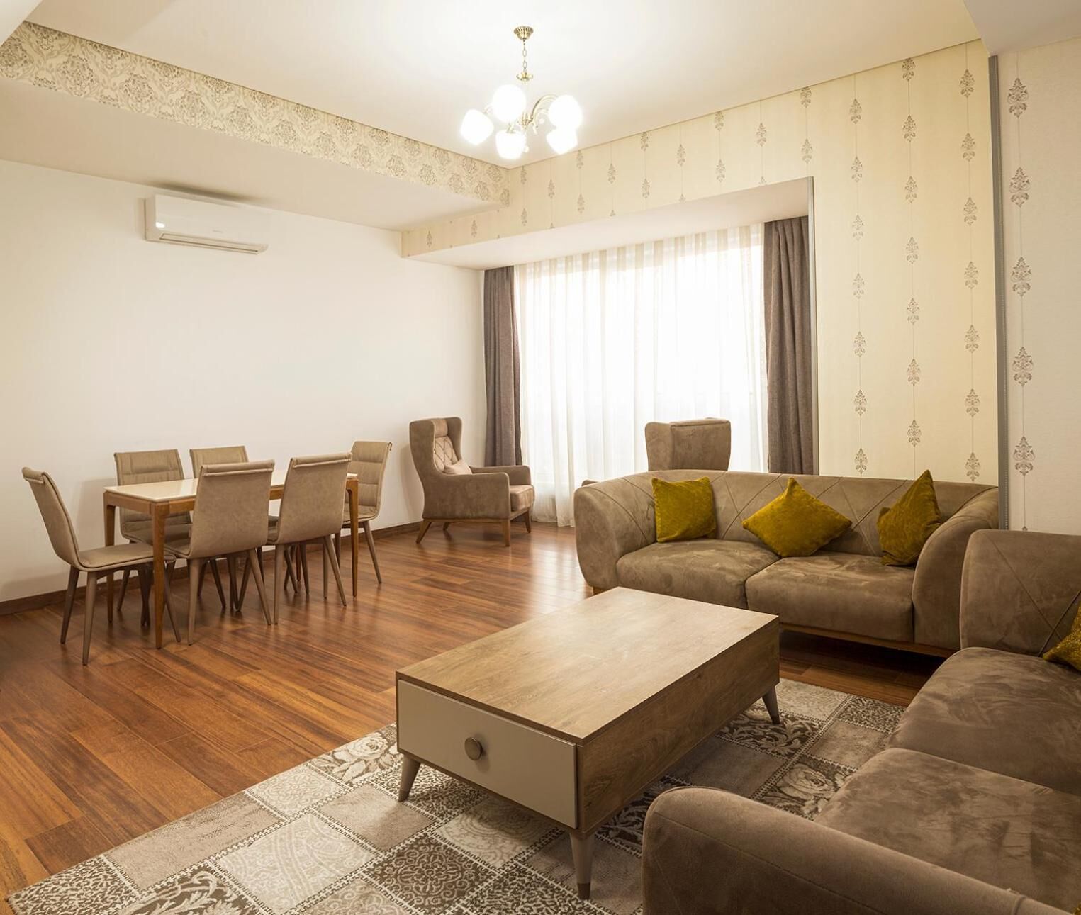 A living room with a sofa, armchairs, a dining table with chairs, a coffee table, and a patterned rug.