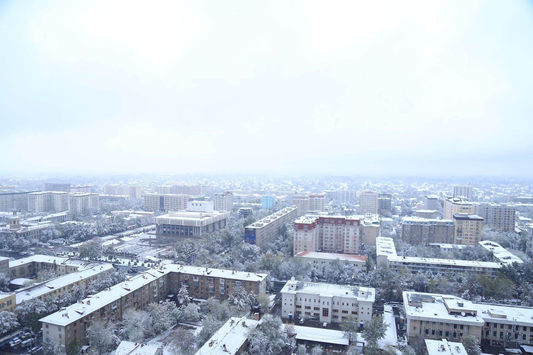 Une vue urbaine avec de nombreux immeubles de grande hauteur, dont certains sont recouverts de neige sur les toits, ce qui indique qu’il s’agit d’un paysage hivernal.