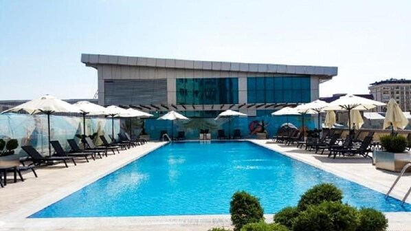 A swimming pool with lounge chairs and umbrellas, surrounded by a modern building with large windows.