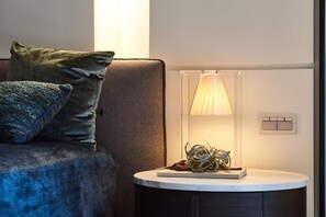 A modern bedroom with a bed, a bedside table with a lamp, and a wall-mounted light switch.
