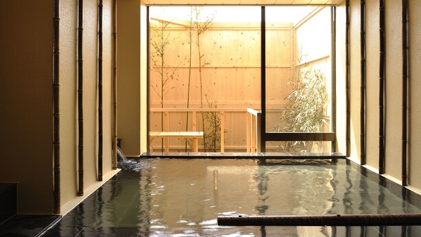 A hot spring bath with a wooden deck and a view of a bamboo garden outside. - Yadoya Tsubaki (Aomori)
